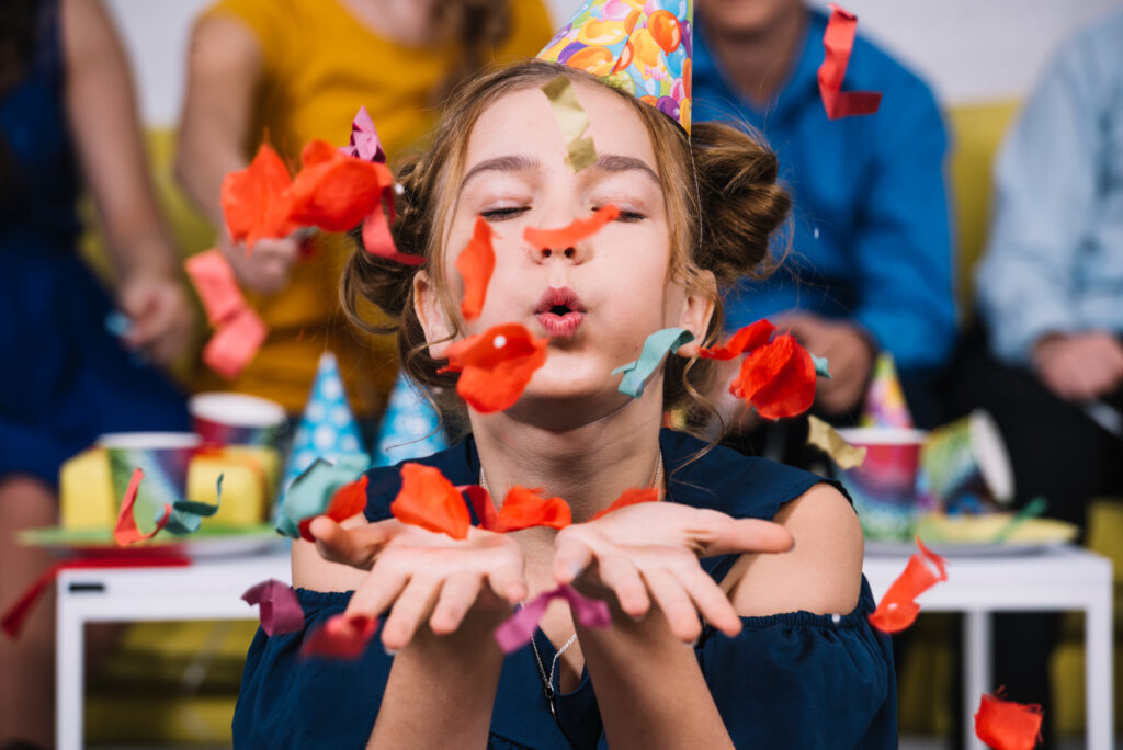 Mädchen pustet Konfetti in die Kamera während einer Kindergeburtstagsfeier